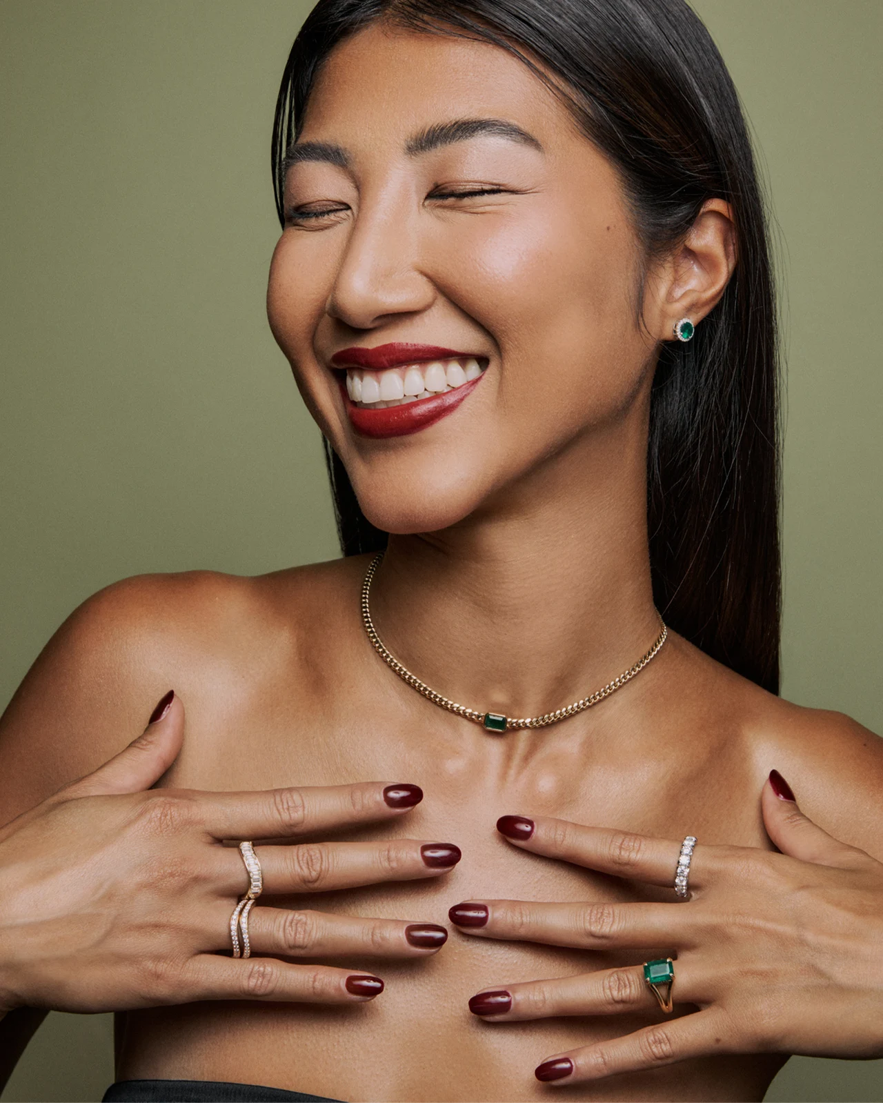 Smiling model with emerald jewelry and deep red nails