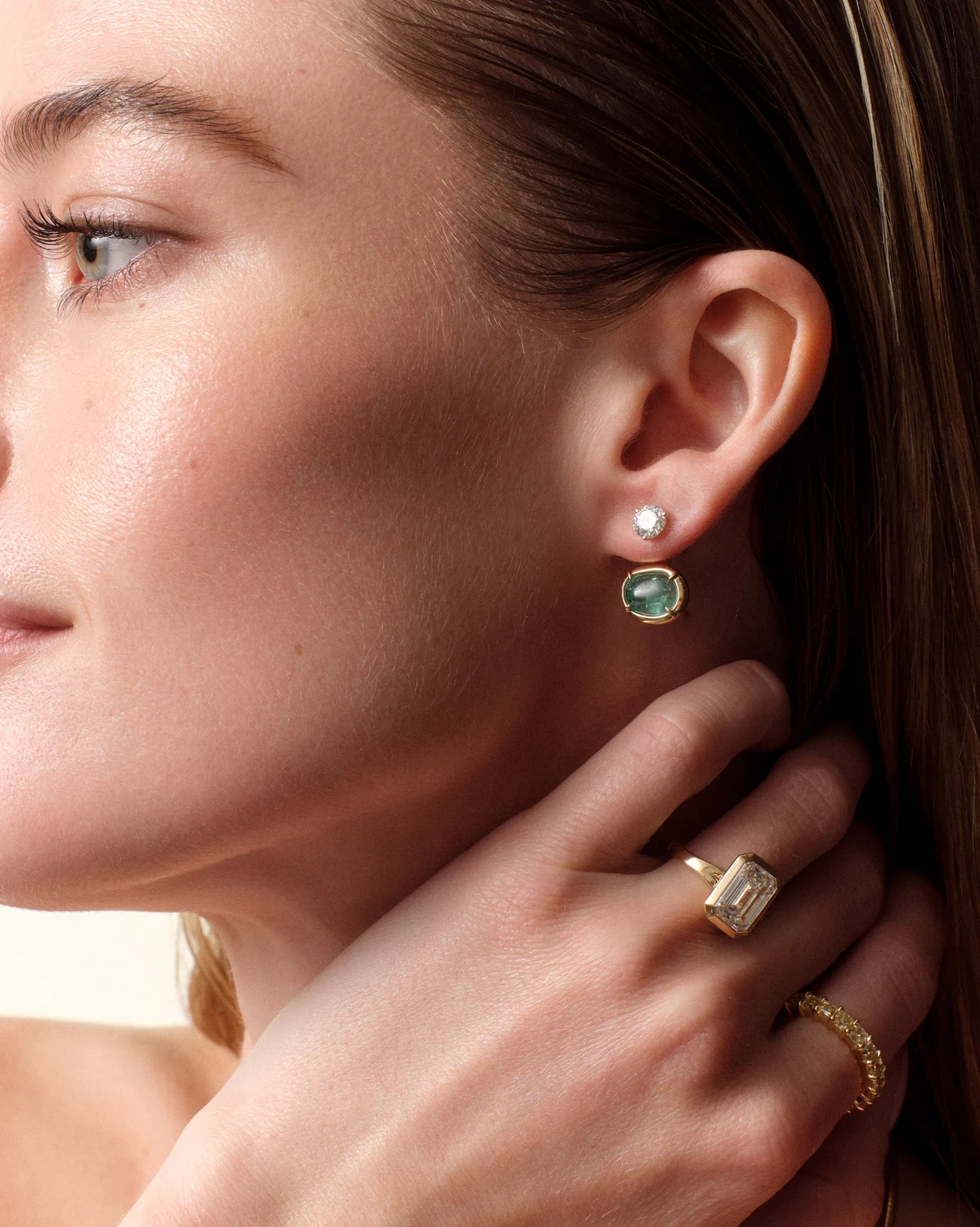 Close-up of a model’s ear, emerald earrings and diamond rings