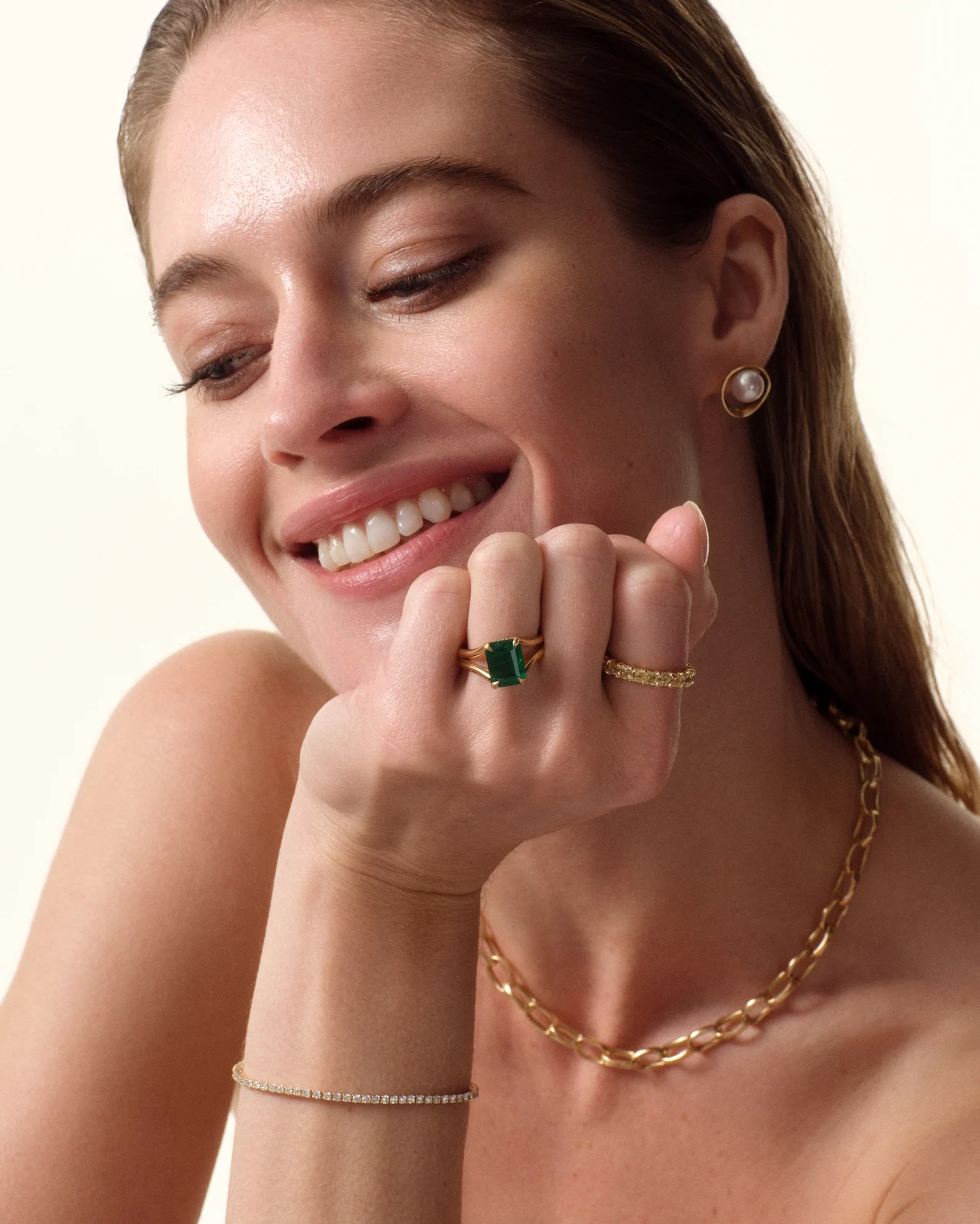 Smiling model wearing gold chains and an emerald ring