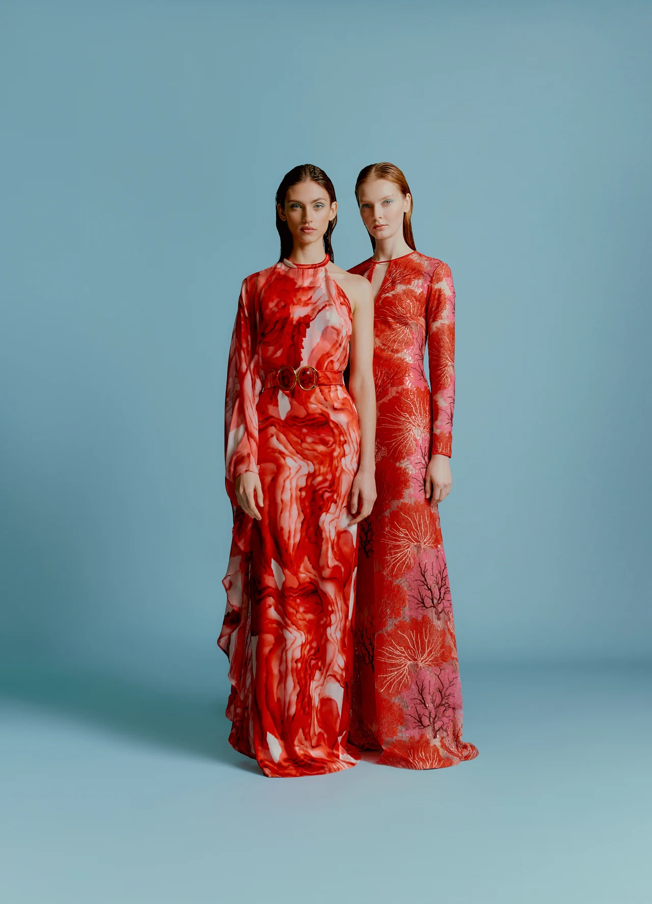 Two models in red floral dresses against a pale blue background